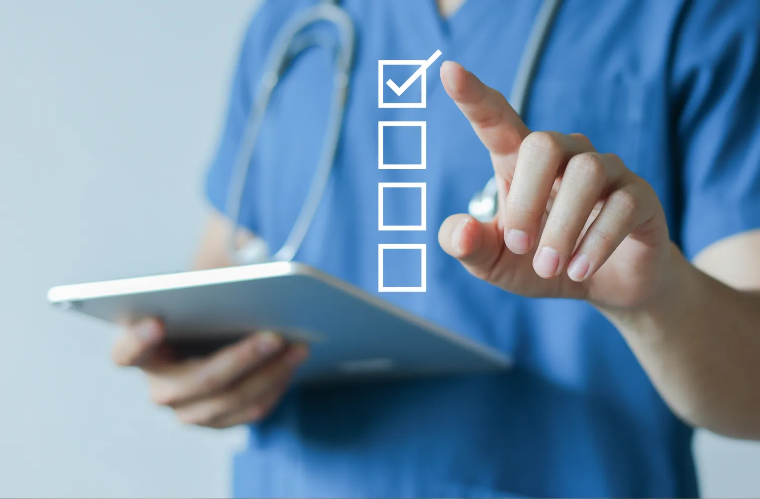 A healthcare professional in blue scrubs, wearing a stethoscope, holds a tablet with one hand and uses the other hand to interact with a virtual checklist featuring a checked box and three unchecked boxes.