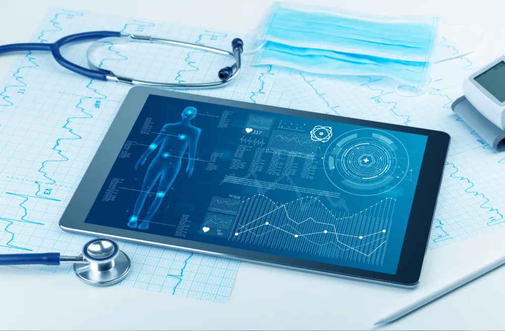 A tablet displaying digital medical data, surrounded by a stethoscope, a disposable face mask, and medical charts.