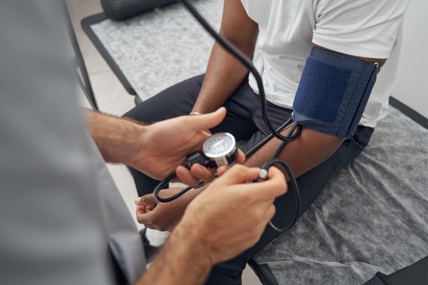 A healthcare professional measures a patient's blood pressure using a sphygmomanometer cuff on the upper arm during a physical exam in a medical clinic.