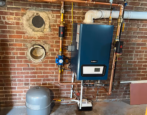 Modern boiler system with pipes mounted on a brick wall and a gray expansion tank on a concrete floor.