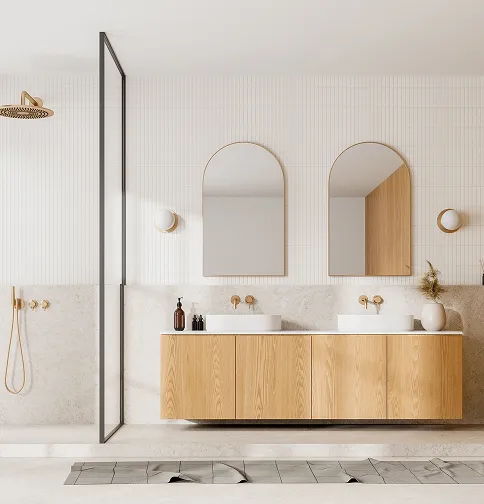Modern bathroom with wooden floating vanity, two oval mirrors, wall-mounted faucets, and a glass shower enclosure with a gold showerhead.