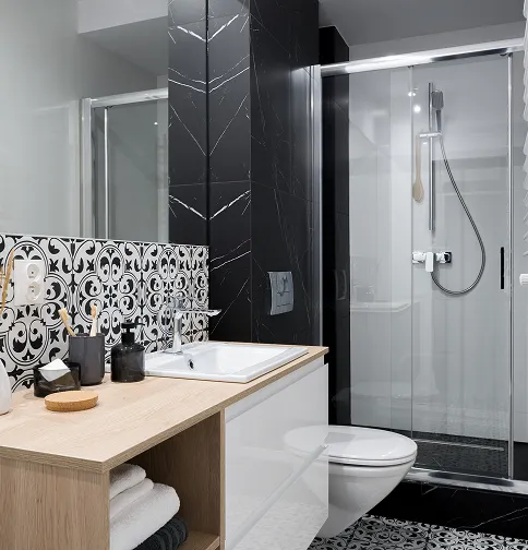 Modern bathroom with a wooden countertop sink, black and white patterned tiles, white toilet, and a glass-enclosed shower with a handheld showerhead.