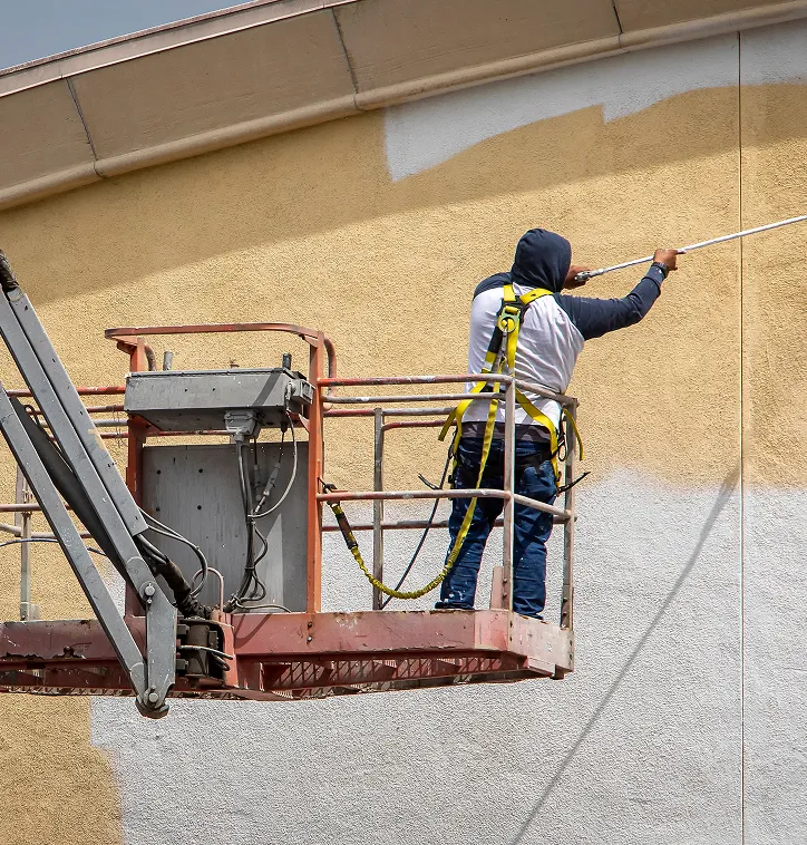 Worker on a hydraulic lift painting a building exterior wall yellow over white.