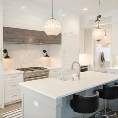 Modern kitchen with white cabinets, marble backsplash, large island with sink, and two black bar stools under hanging glass pendant lights.