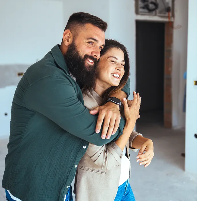 Smiling couple embracing warmly inside a room under renovation.