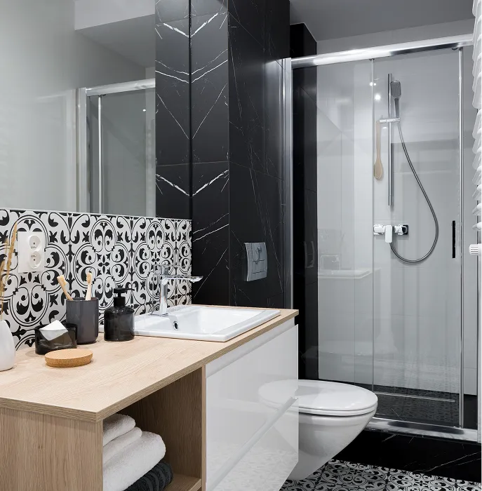 Modern bathroom with wooden countertop sink, black and white patterned tiles, toilet, and glass-enclosed shower.