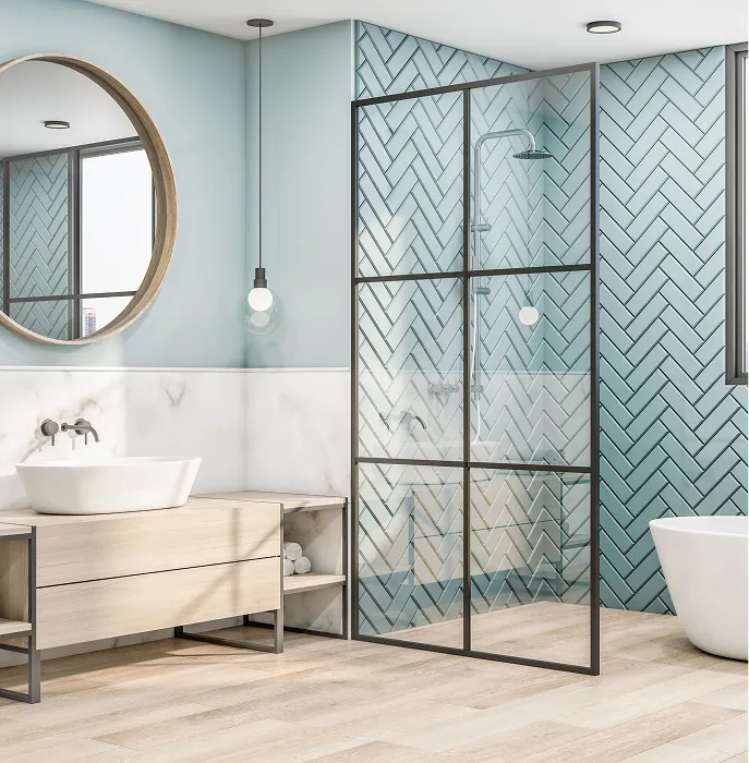 Modern bathroom with light wood vanity, round mirror, glass shower with blue herringbone tiles, and a freestanding white bathtub.