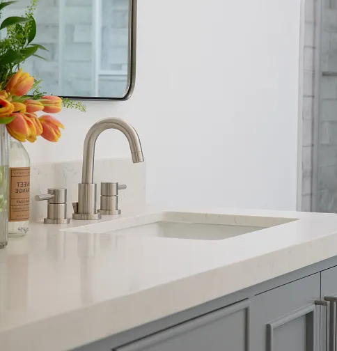 Modern bathroom sink with a stainless steel faucet and orange tulips in a glass vase on the countertop.