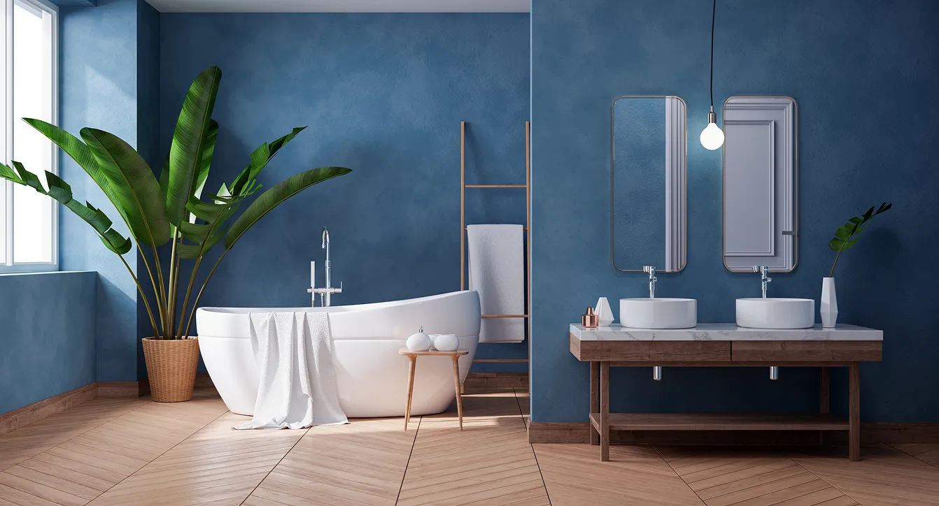 Modern blue bathroom with a freestanding tub, wood vanity, and plant accents after renovation services.