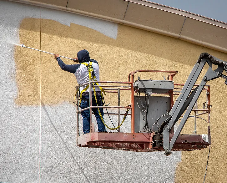 Contractor using lift to repaint commercial building exterior as part of renovation services.