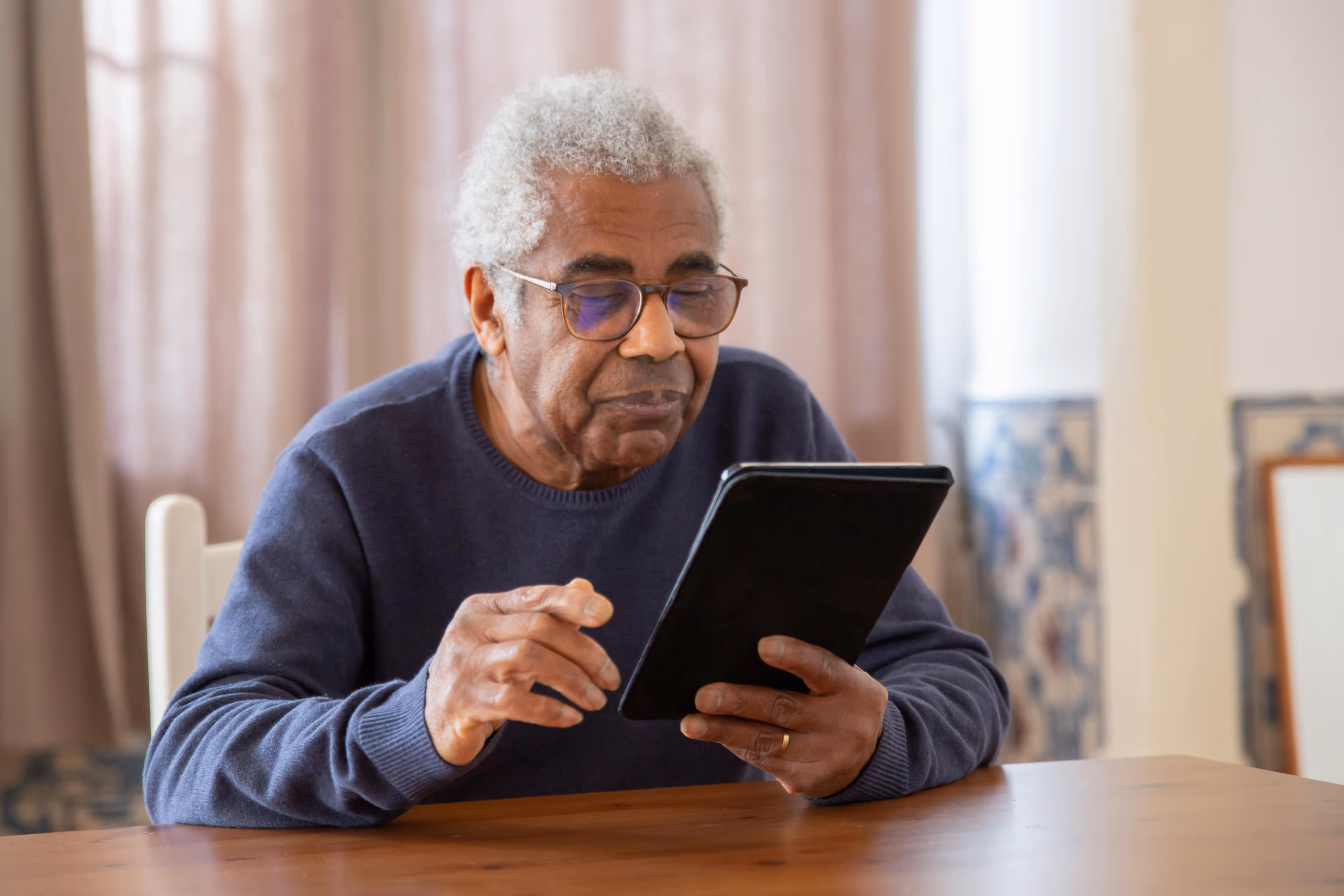 An older man is focused on using a tablet computer, sitting comfortably in a well-lit room.