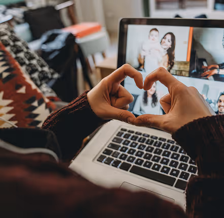 A person forms a heart shape with their hands while sitting in front of a laptop.