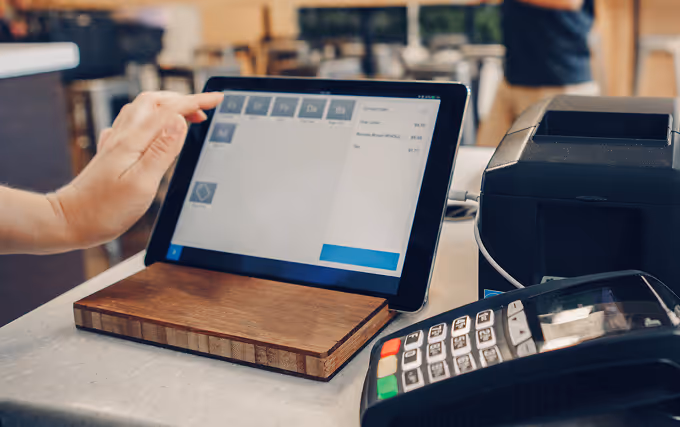 A person using a tablet to complete a payment for their coffee at a café.