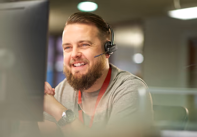 A bearded man wearing a headset sits in front of a computer, focused on his work.