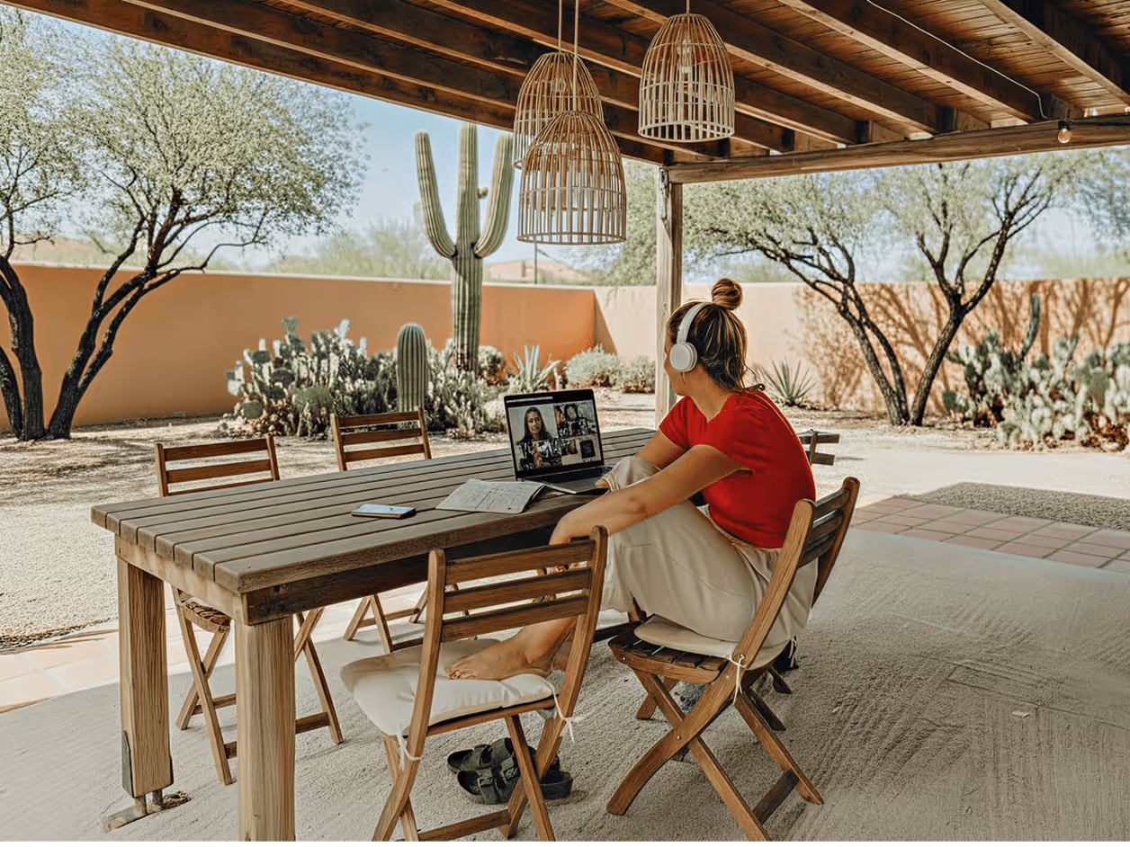 A woman working from home in Arizona, seated at a desk with a laptop and a view of the desert landscape outside.