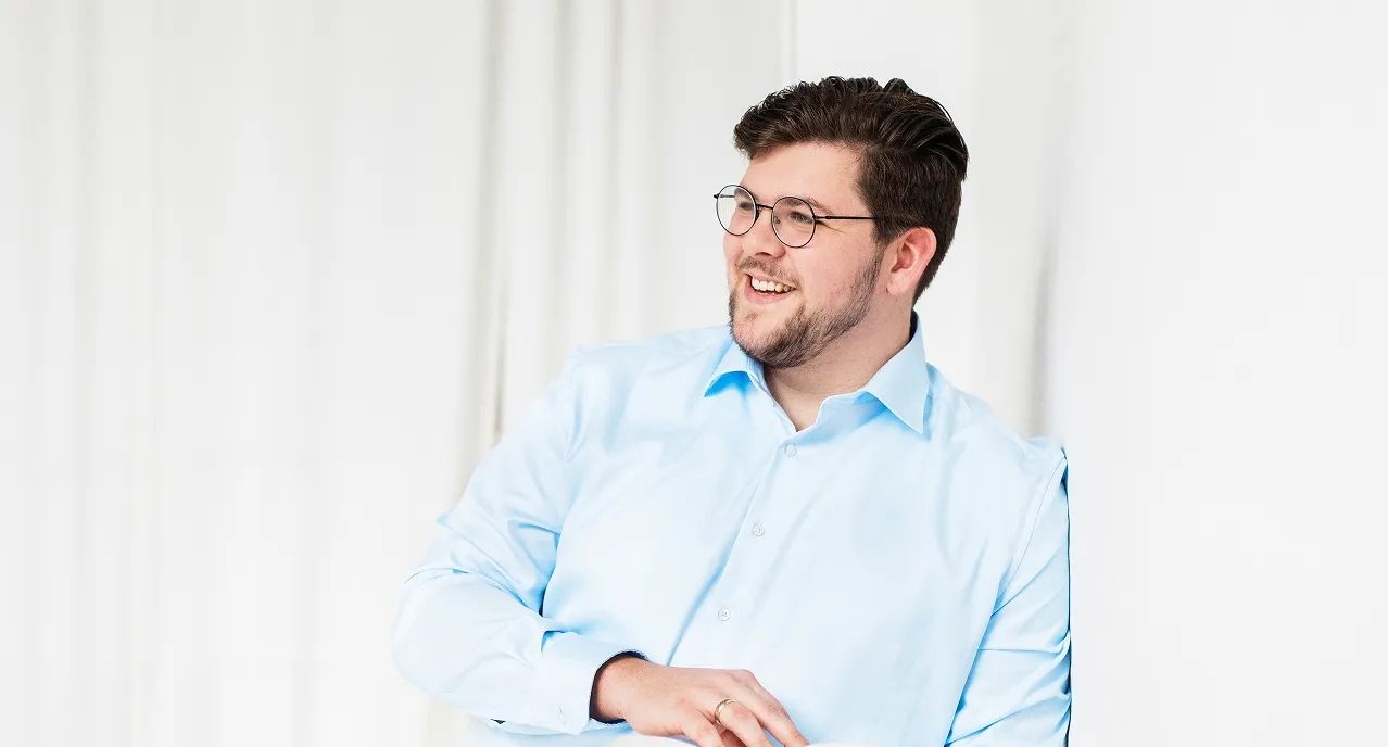 Smiling man with glasses and beard wearing a light blue dress shirt looking to the right.
