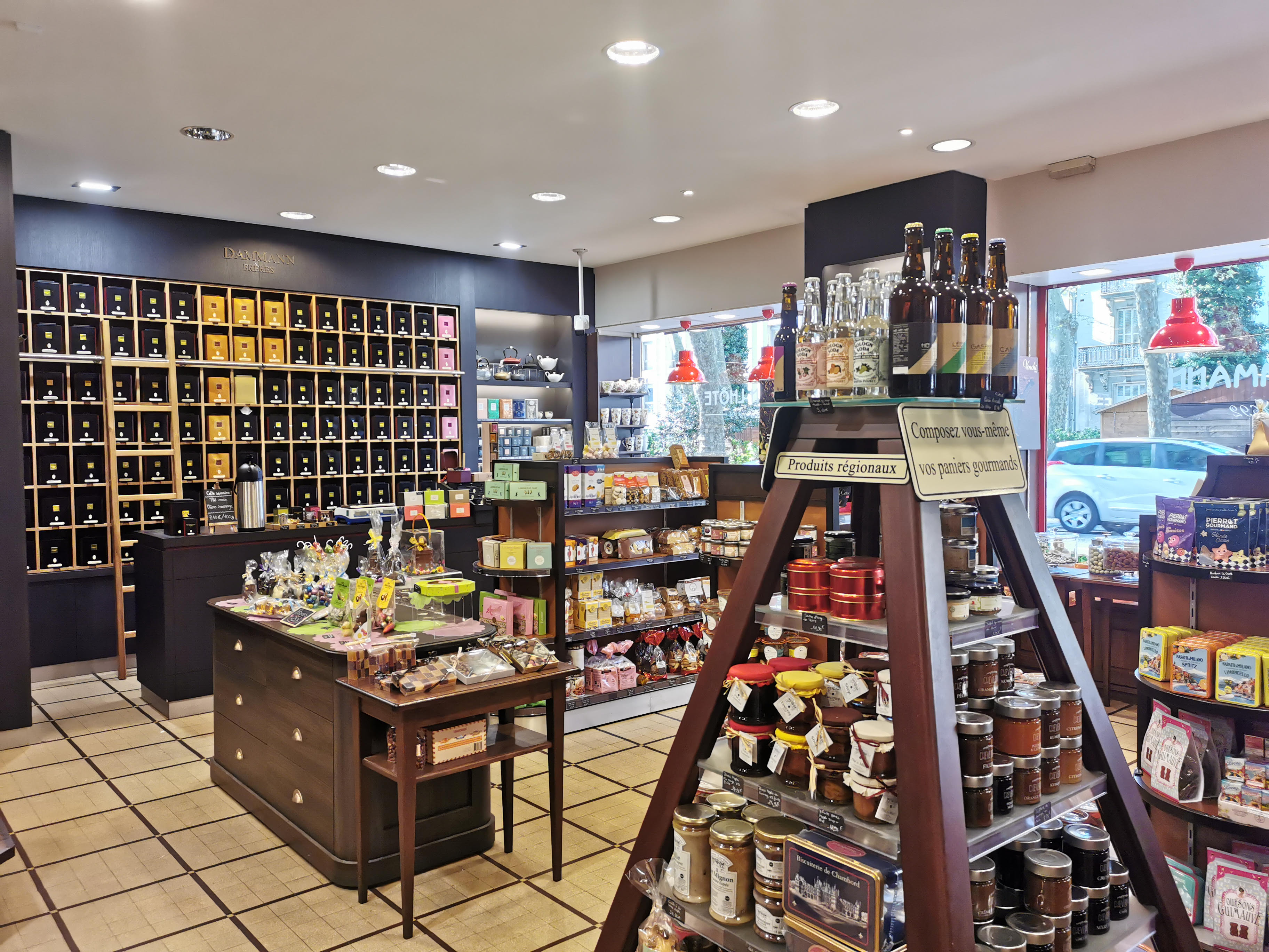 Intérieur de la boutique Maison Lhôte à Tours avec des étagères présentant du thé, des confitures, des boissons en bouteille et des confiseries emballées, disposés sur des meubles en bois.