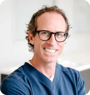 Smiling man with glasses wearing a blue medical scrub top.