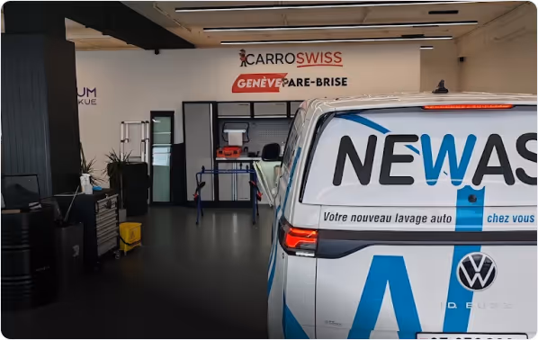 Intérieur d'un atelier automobile avec une camionnette blanche New Wash garée, signalée comme service de lavage auto à domicile.