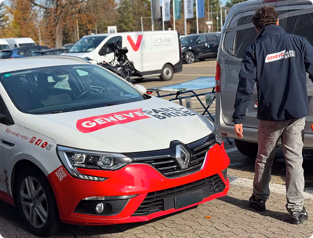 Voiture blanche et rouge avec le logo Genève Aéroport et un homme portant une veste assortie debout près d'une autre voiture grise dans un parking.