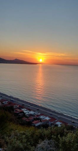 Sonnenuntergang über ruhigem Meer mit Blick auf eine Küstenstraße und Häuser im Vordergrund.