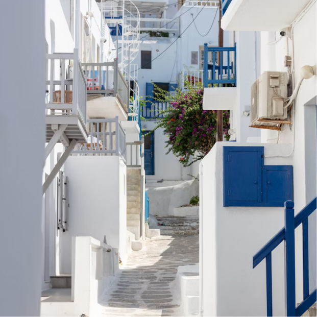 Enge Gasse mit weiß getünchten Gebäuden und blauen Türen und Geländern, typisch für eine griechische Insel.
