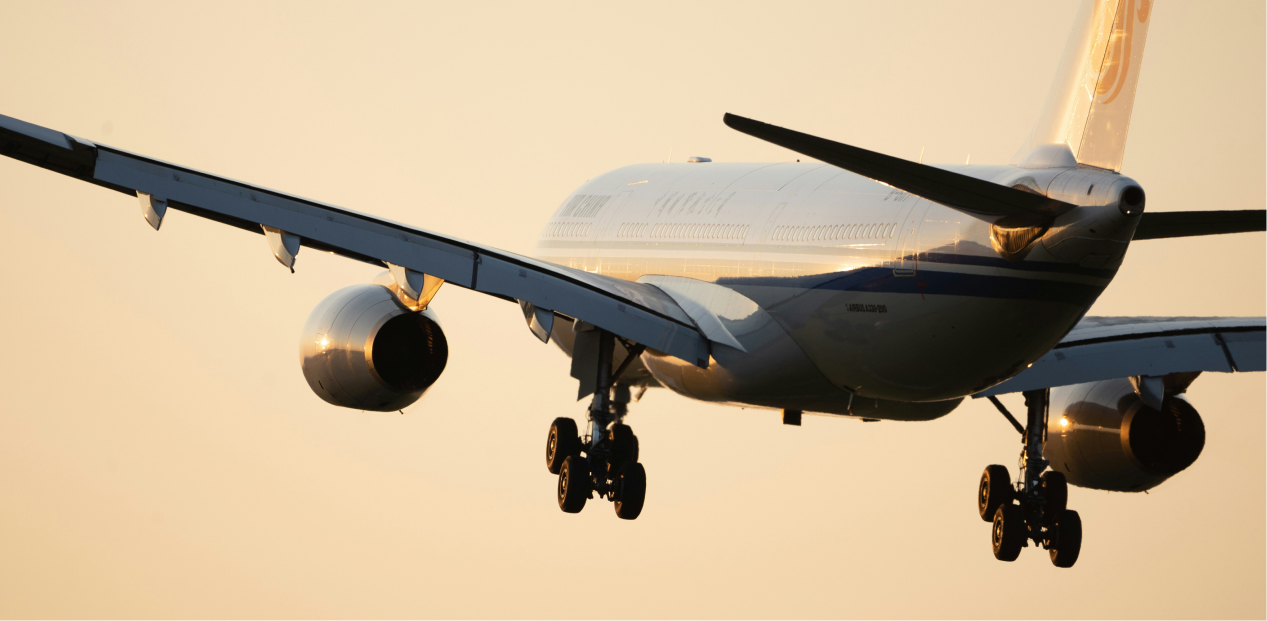 Passagierflugzeug im Landeanflug bei Sonnenuntergang mit ausgefahrenem Fahrwerk.