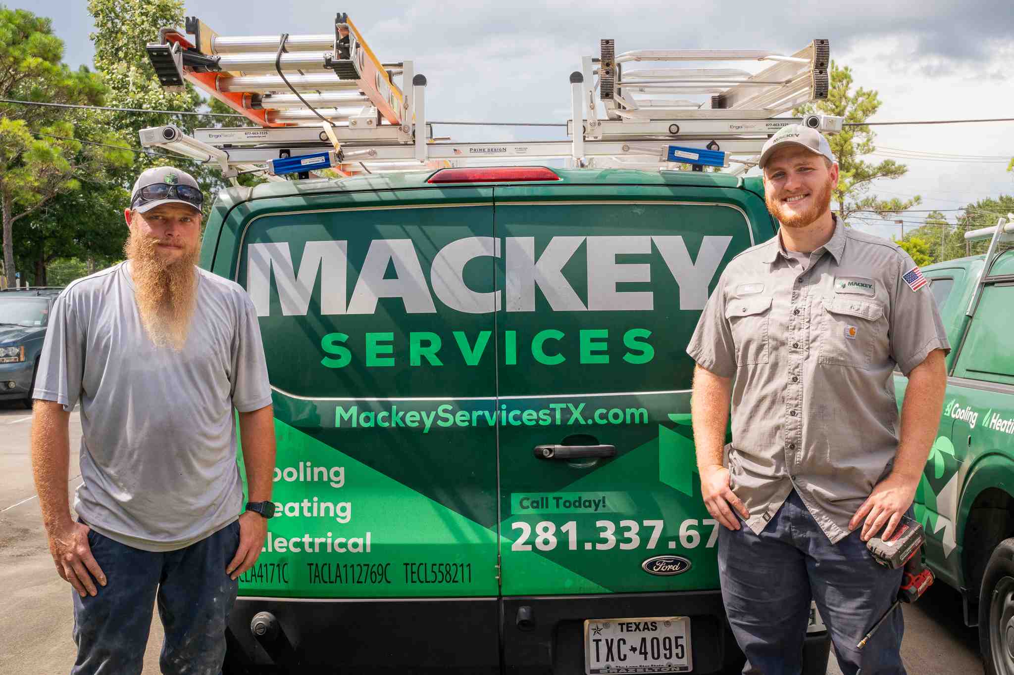 Two men standing in front of a green Mackey Services van with ladders on top and company contact information.