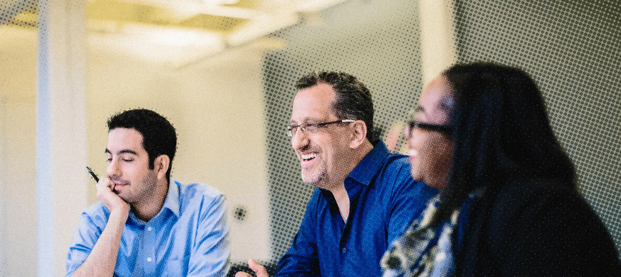 Three colleagues smiling and conversing in a bright office setting.
