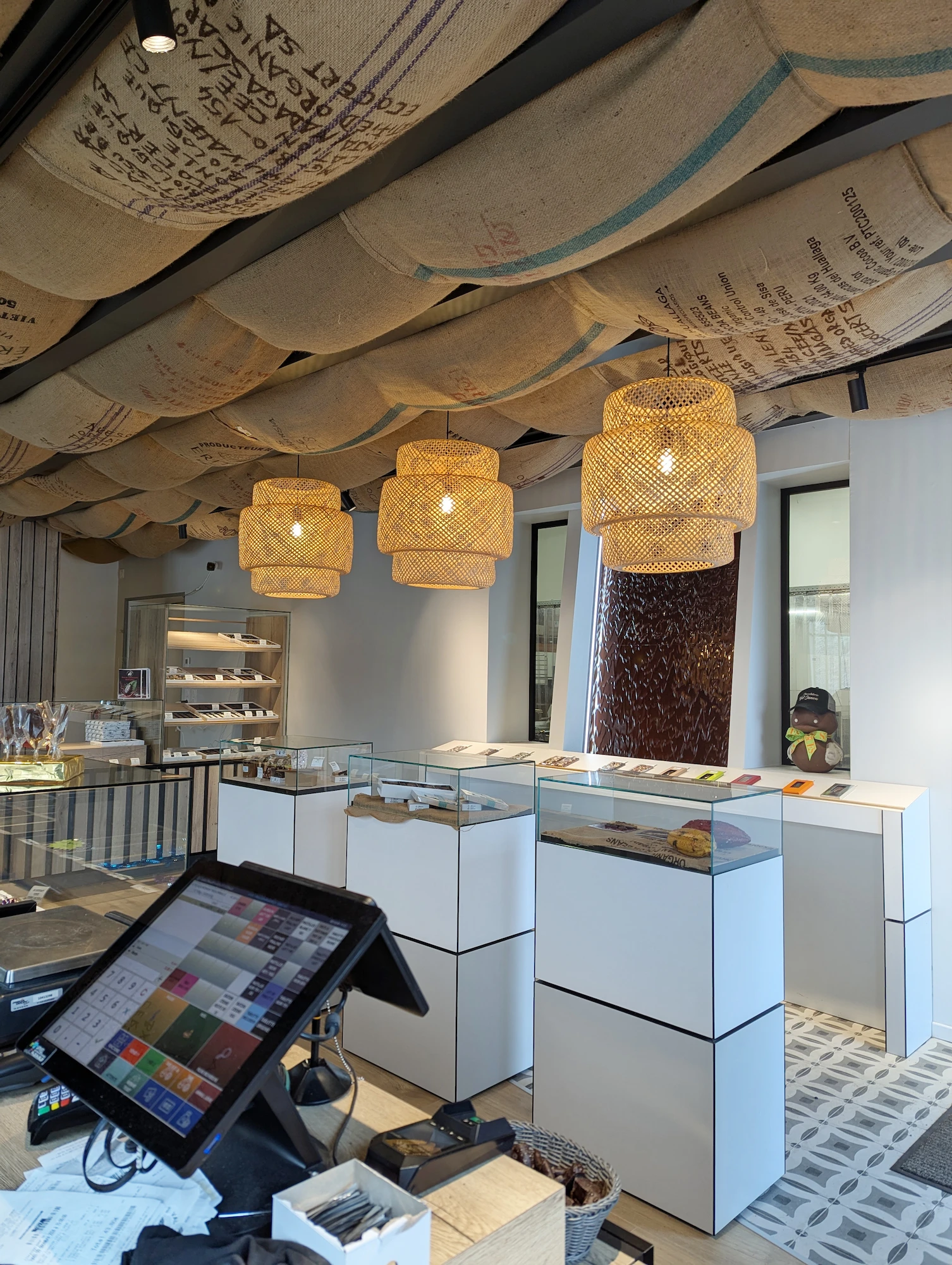 Espace de vente de la chocolaterie conçu par l'agence Jiwa.A, avec suspensions en osier et vitrines d’exposition.