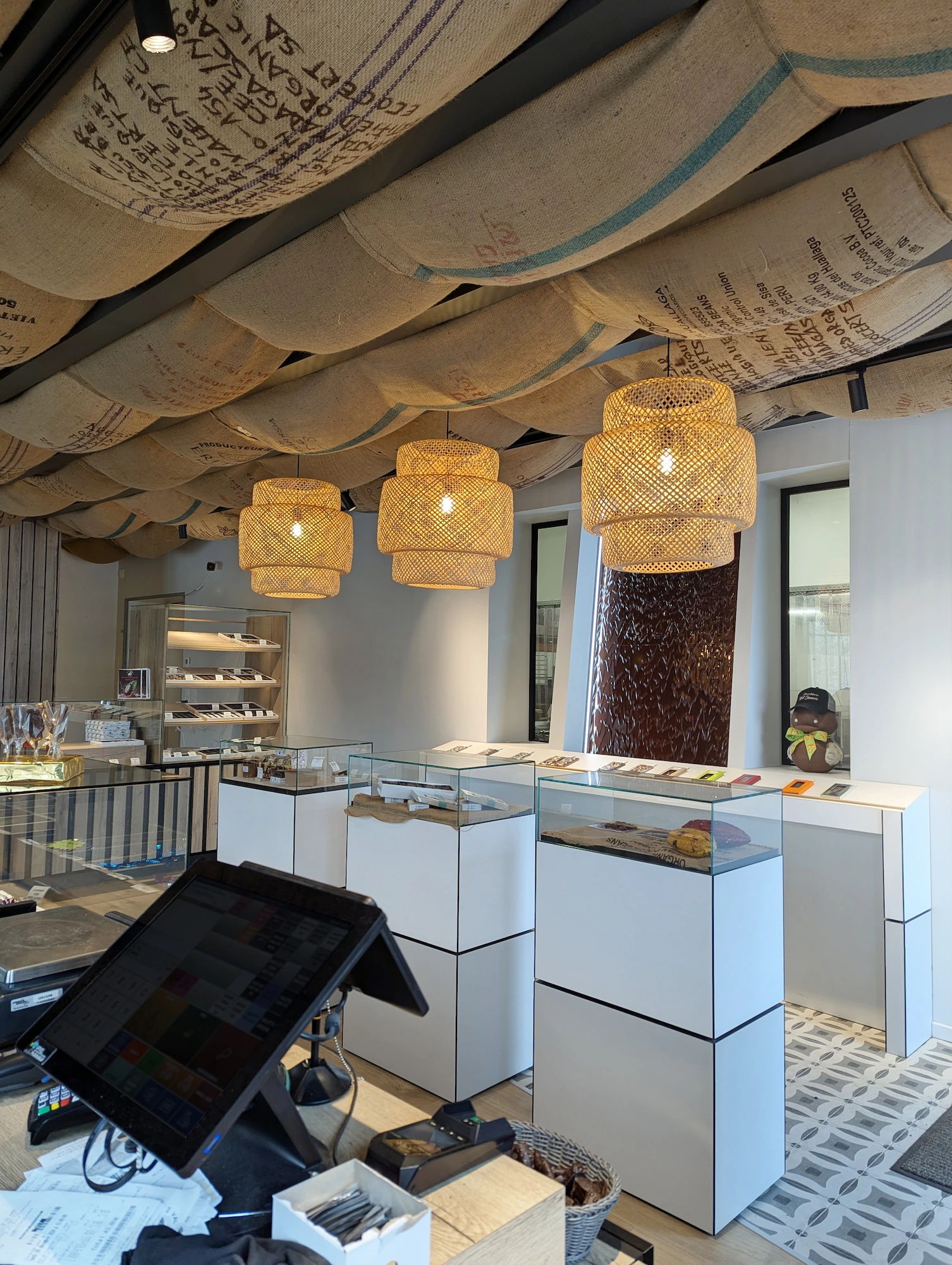 Zone de présentation de la chocolaterie Val Janon avec luminaires en osier et mobilier blanc imaginés par Valentine.