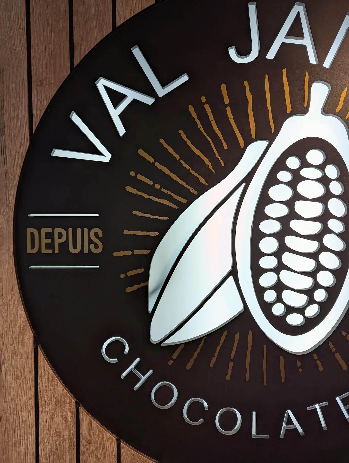 Gros plan sur le logo de la chocolaterie Val Janon fixé sur un mur en bois.