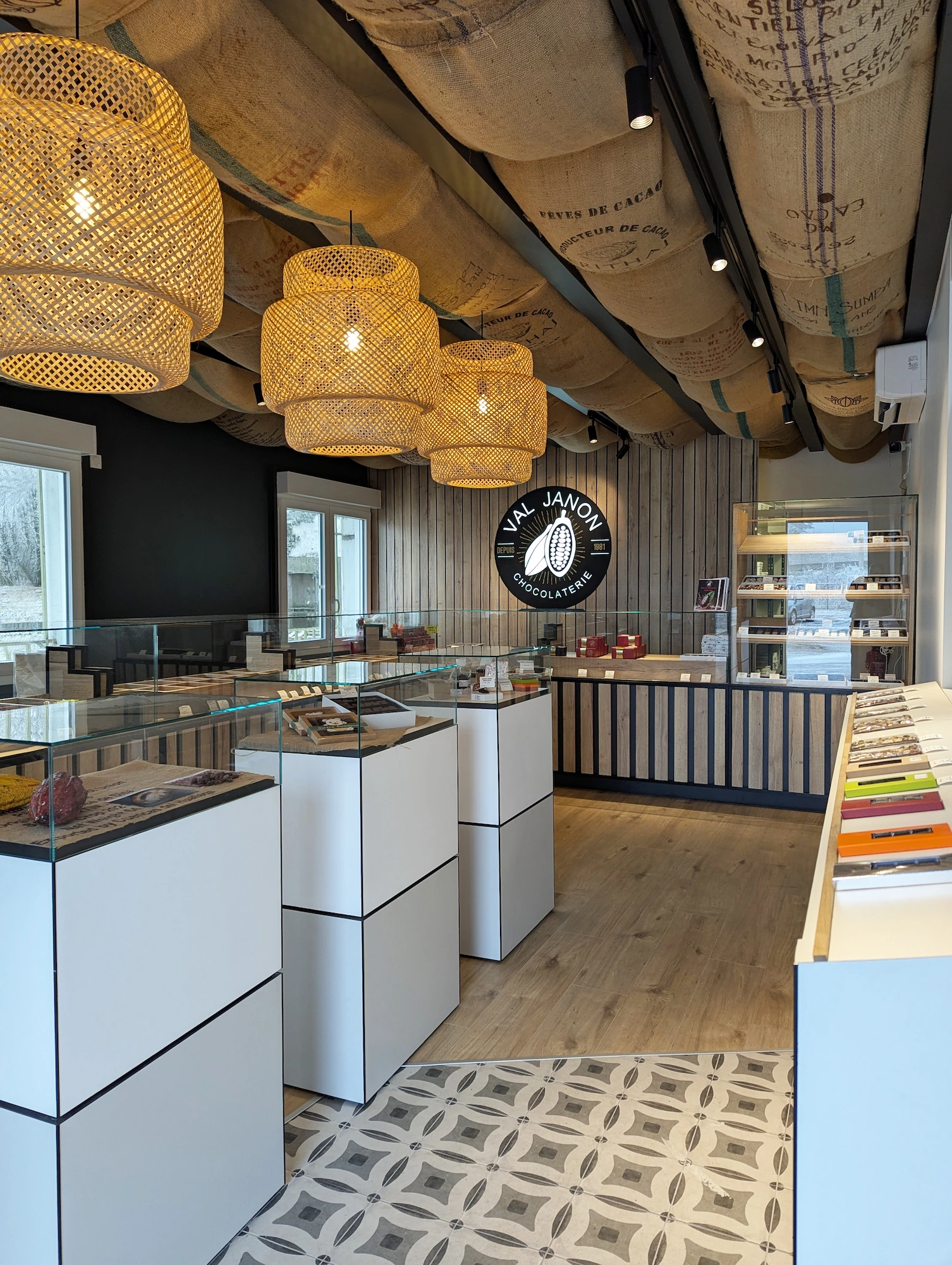 Vue d’ensemble de la chocolaterie Val Janon : luminaires en fibres naturelles, mobilier blanc et décor chaleureux