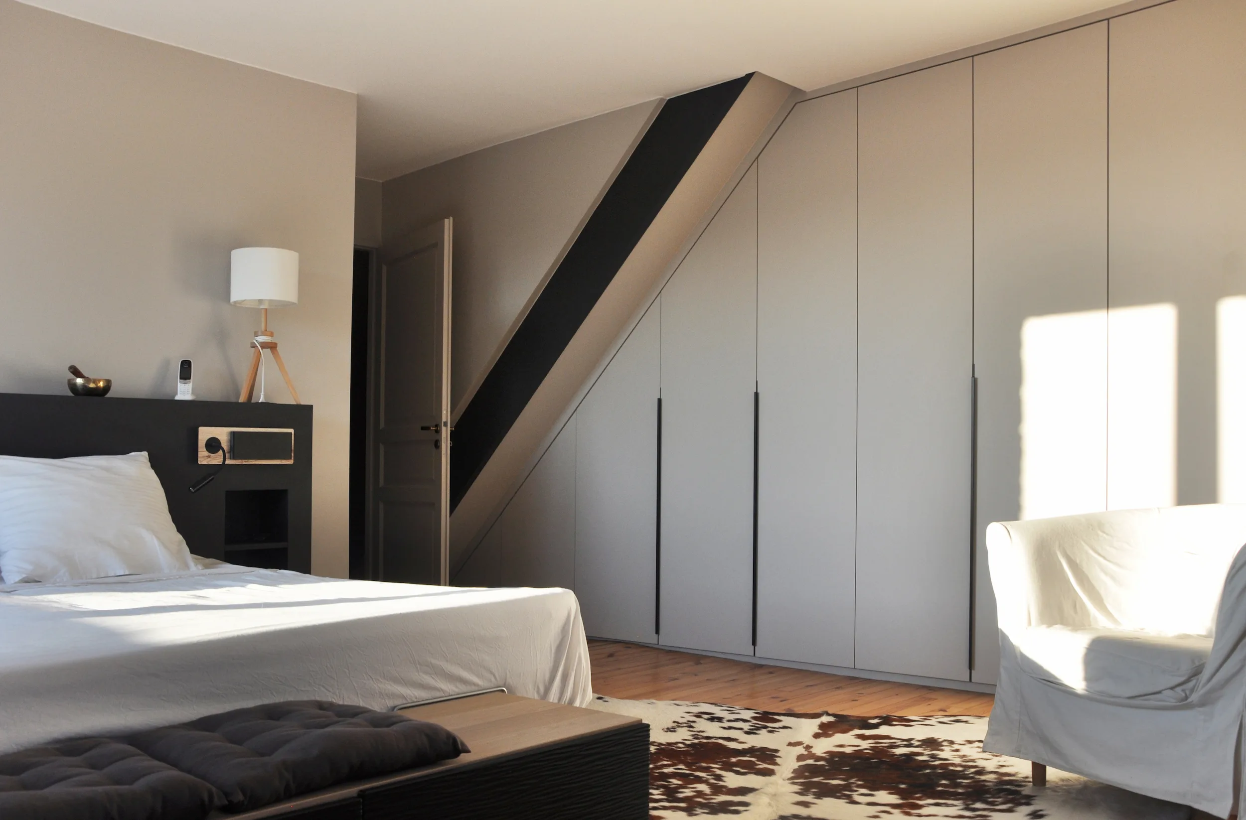Chambre contemporaine baignée de lumière, avec grands rangements intégrés et lignes minimalistes conçues pour optimiser un espace mansardé.