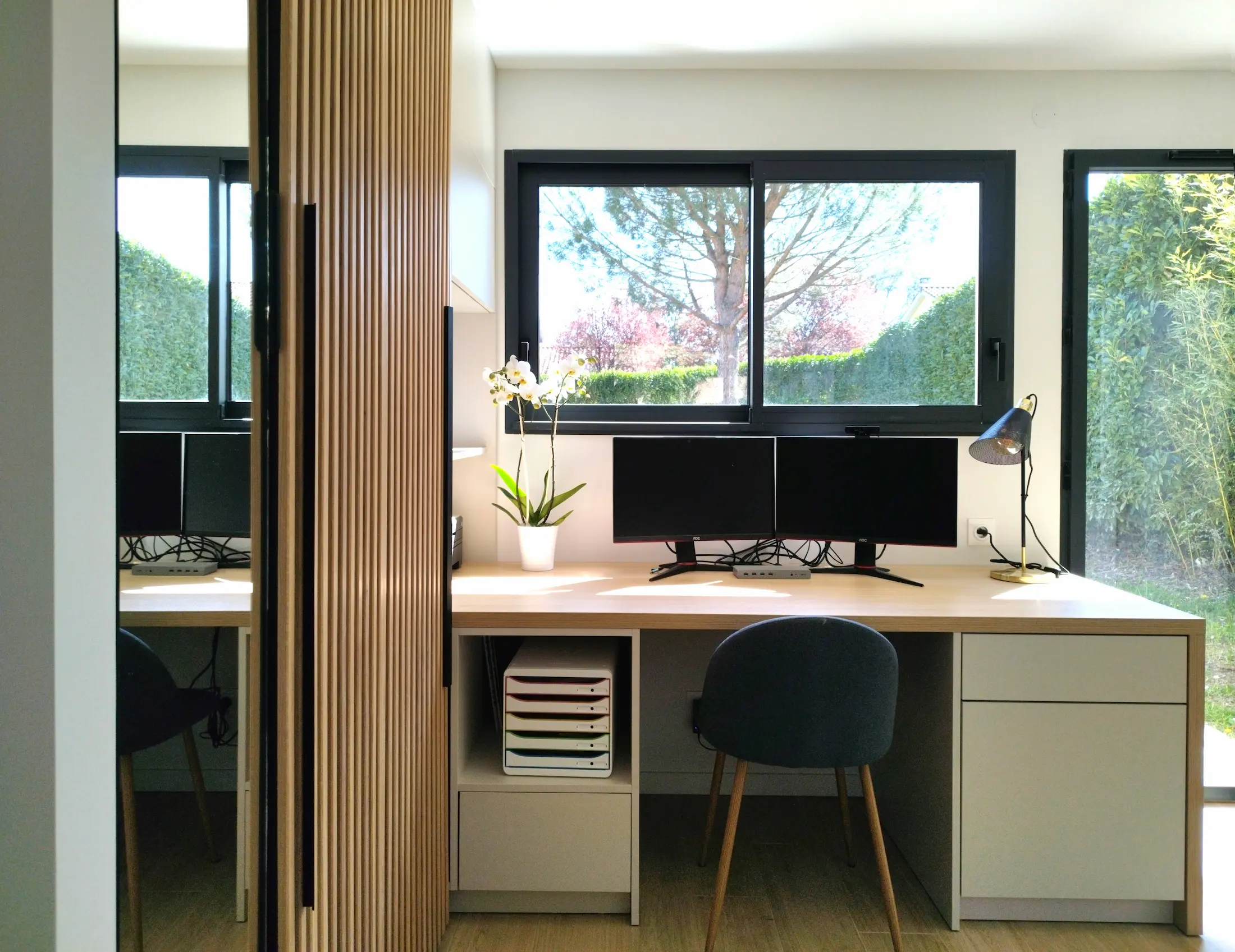 Espace de travail lumineux avec double écran et vue sur le jardin.