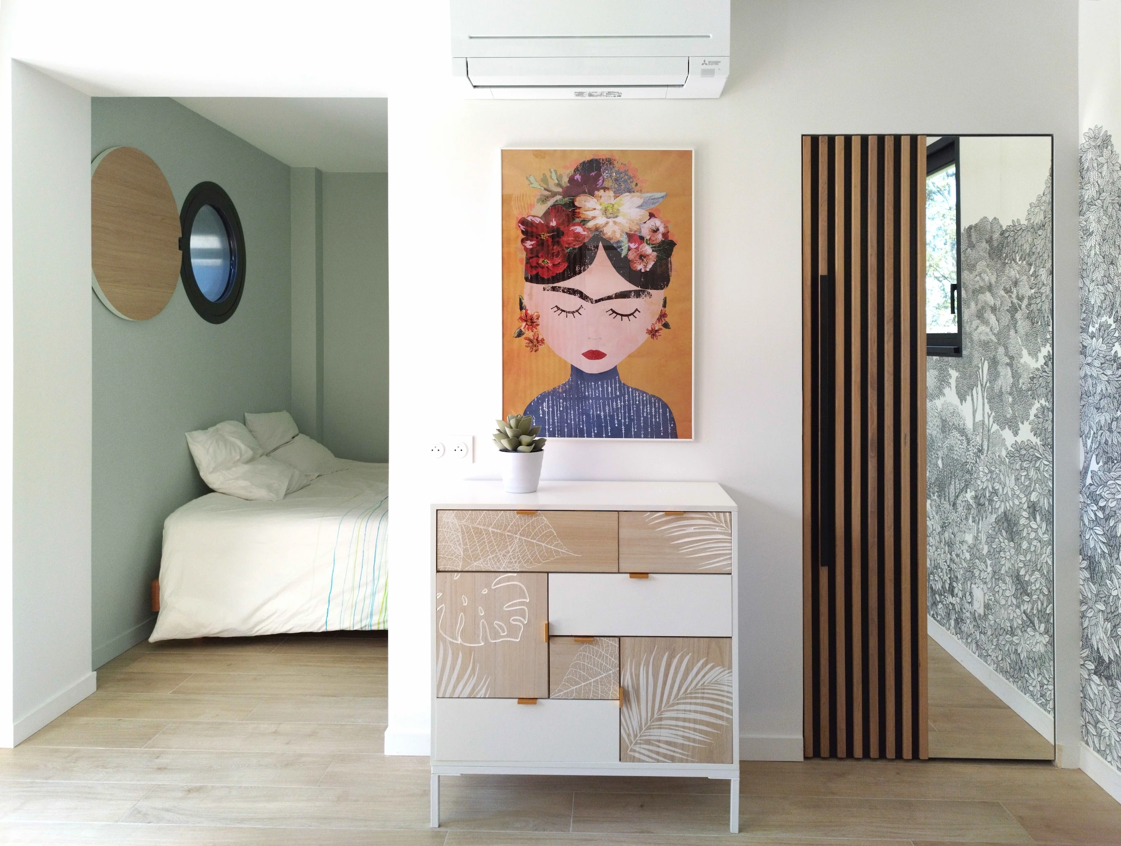 Intérieur d’une chambre contemporaine avec commode décorative, œuvre colorée, miroir vertical et coin nuit séparé