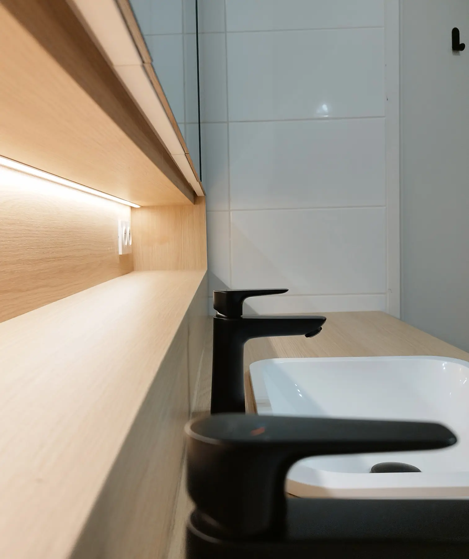 Gros plan sur les robinets noirs et l’éclairage sous meuble du projet salle de bain signé Jiwaa.
