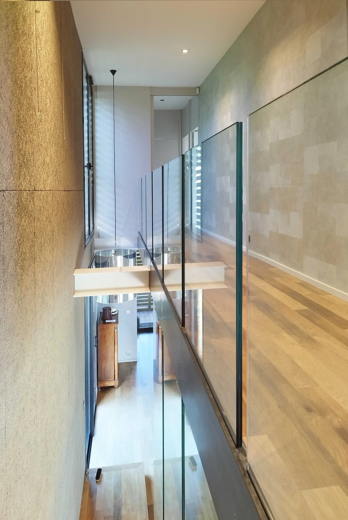 Couloir contemporain avec garde-corps en verre et parquet en bois clair, favorisant la circulation de la lumière.