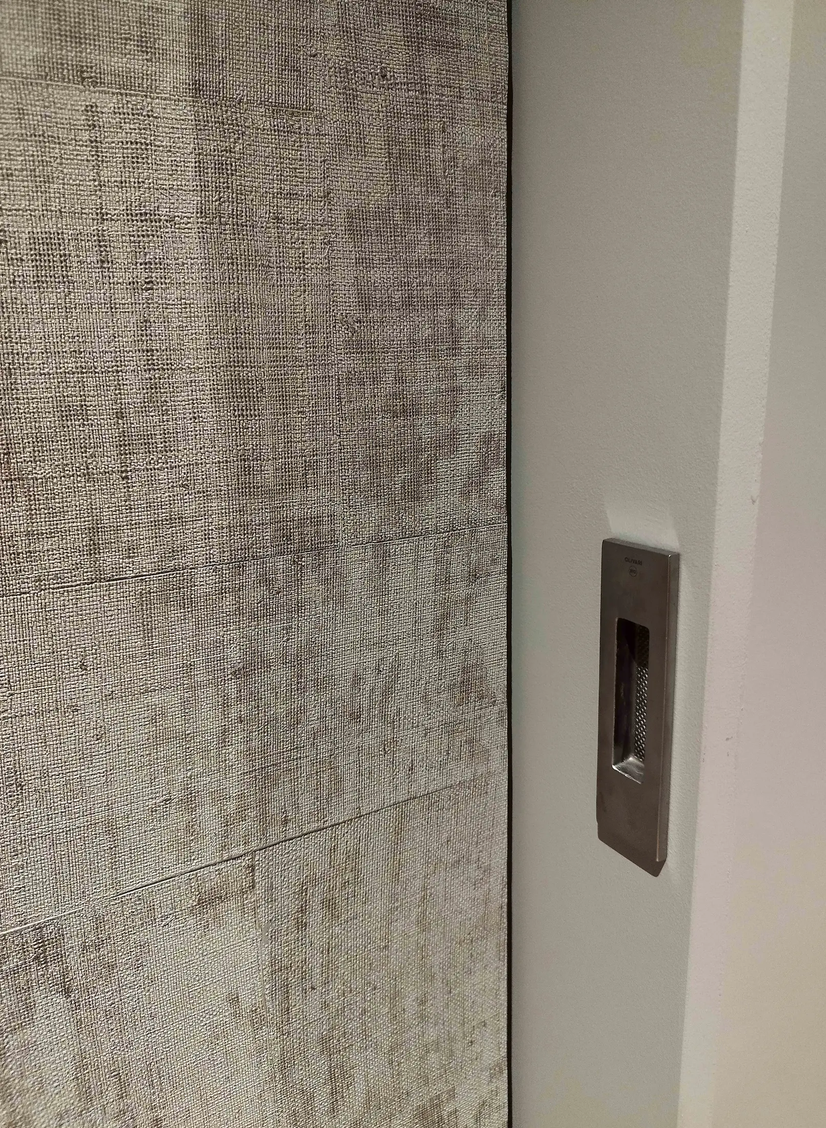Détail de porte coulissante intégrée et revêtement mural texturé, dans un intérieur contemporain rénové.