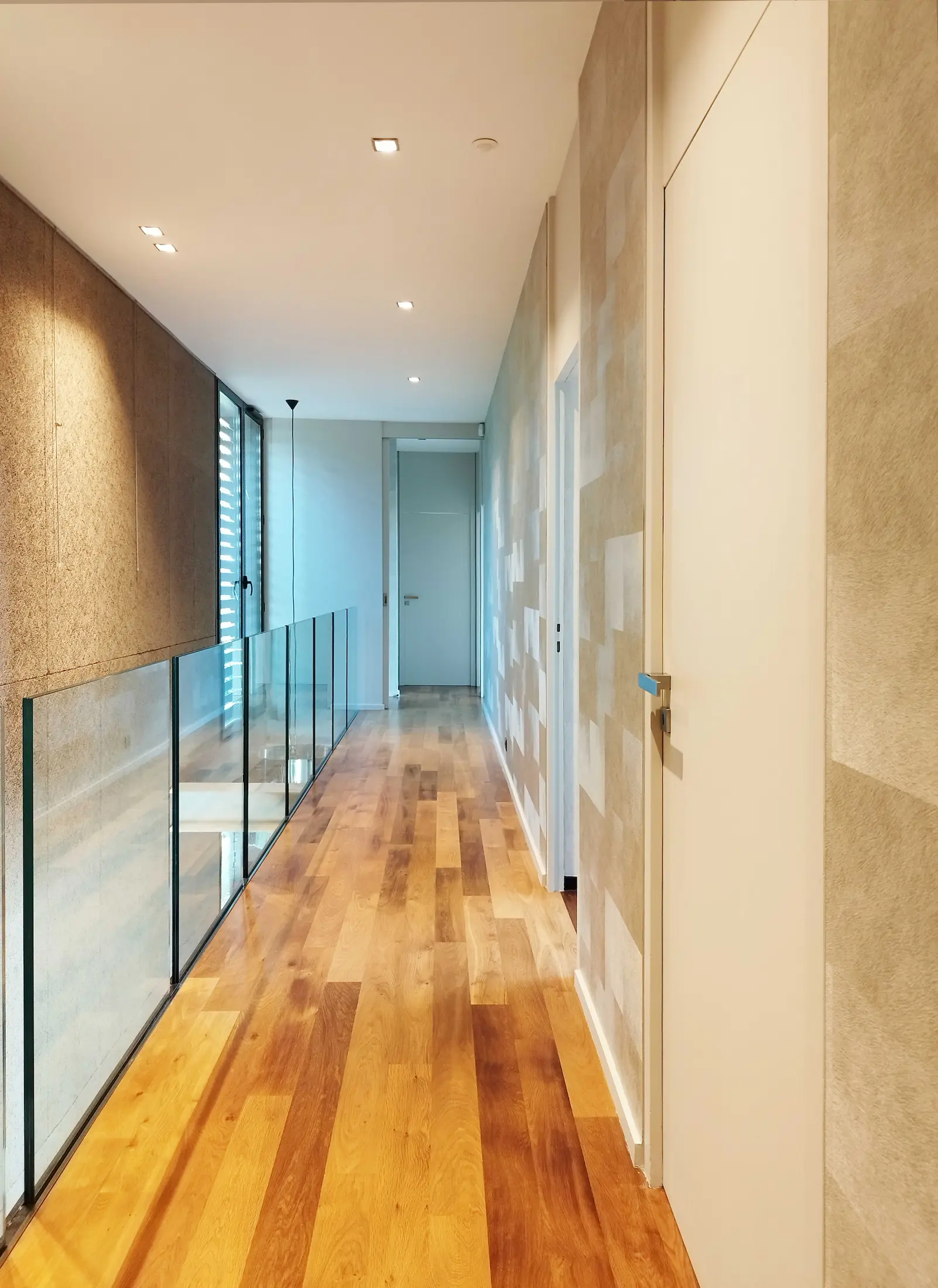 Couloir moderne avec portes blanches, sol en bois et revêtements muraux texturés, conçu pour optimiser la luminosité intérieure.