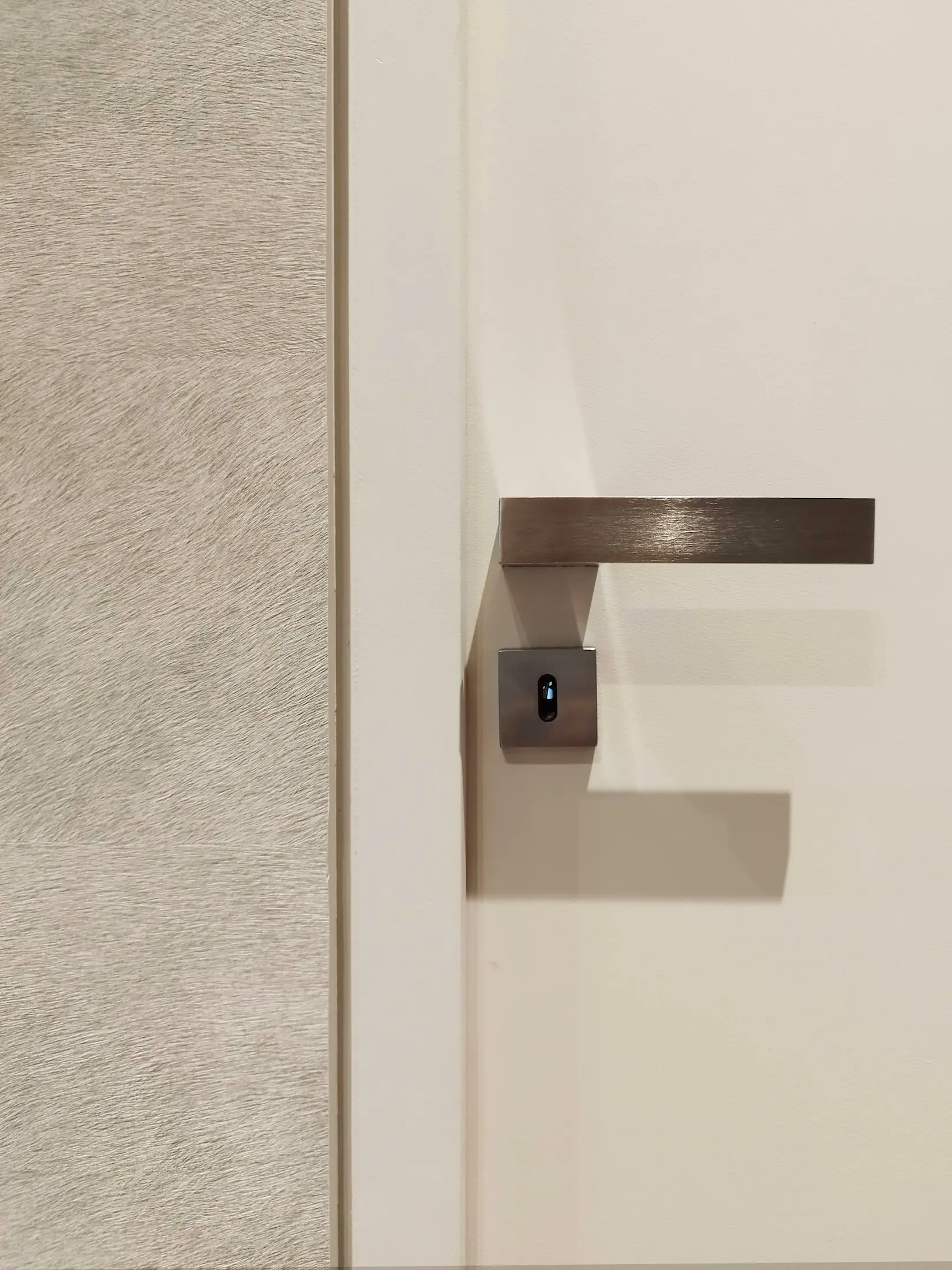 Détail de poignée de porte minimaliste sur mur texturé, dans un couloir contemporain aux tons clairs.