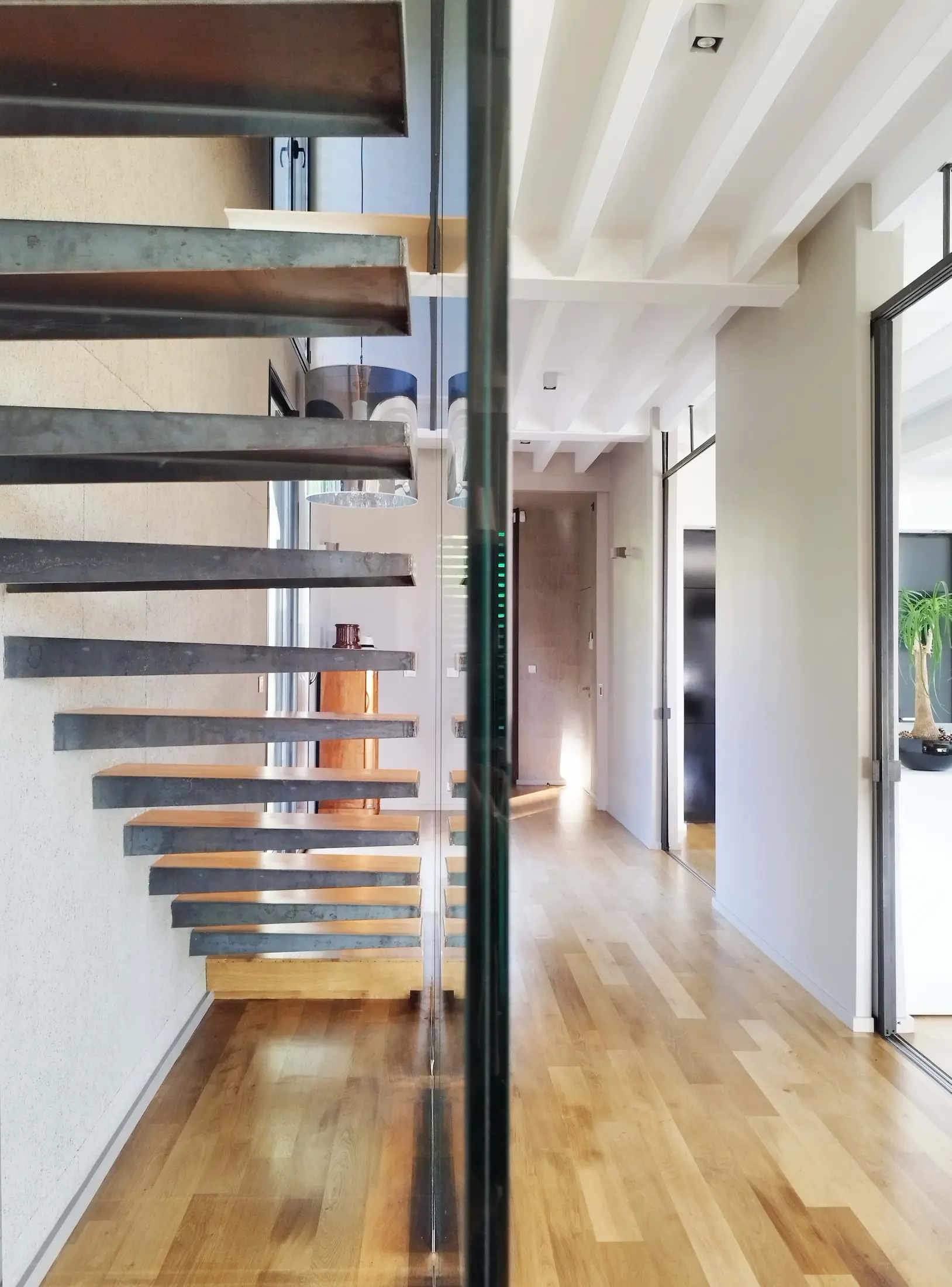 Détail de l’escalier contemporain avec marches en bois et garde-corps en verre.
