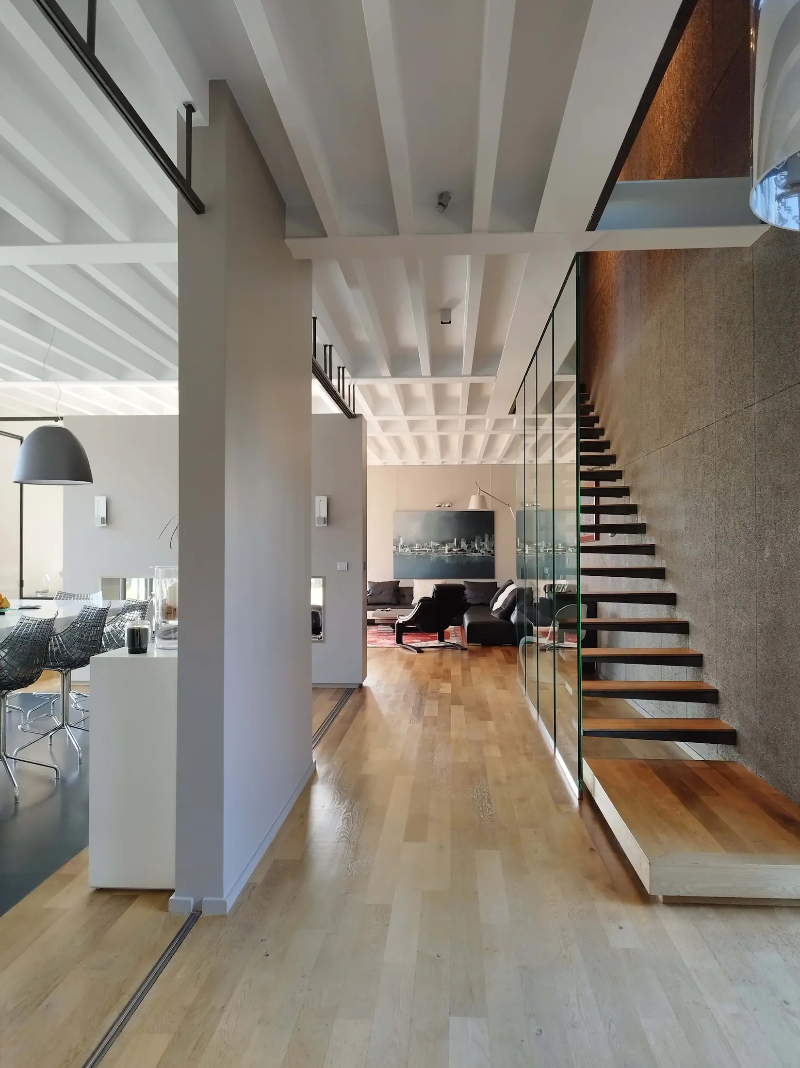 Salon contemporain lumineux avec escalier en bois et garde-corps en verre.