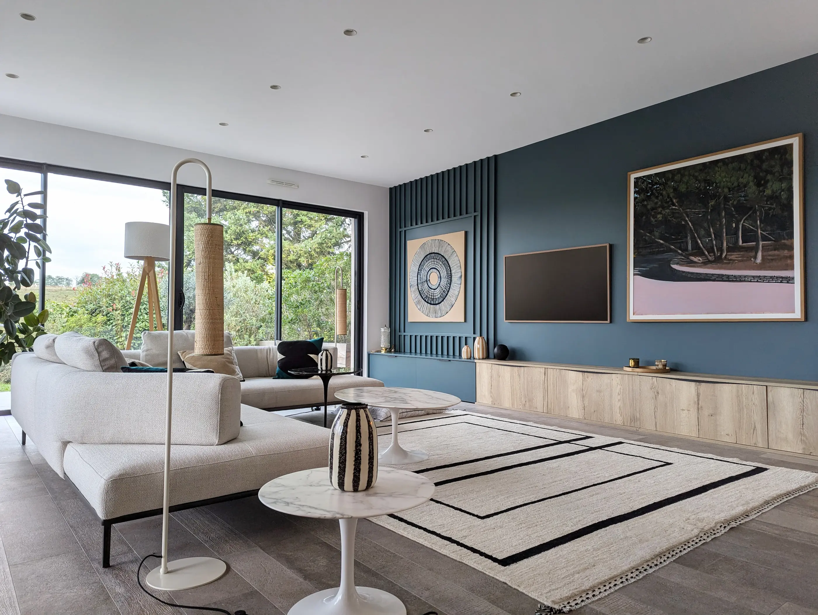 Salon contemporain avec grande baie vitrée, murs bleu profond, meubles sur mesure en bois clair et décoration minimaliste, dans un intérieur imaginé autour des tasseaux de bois.