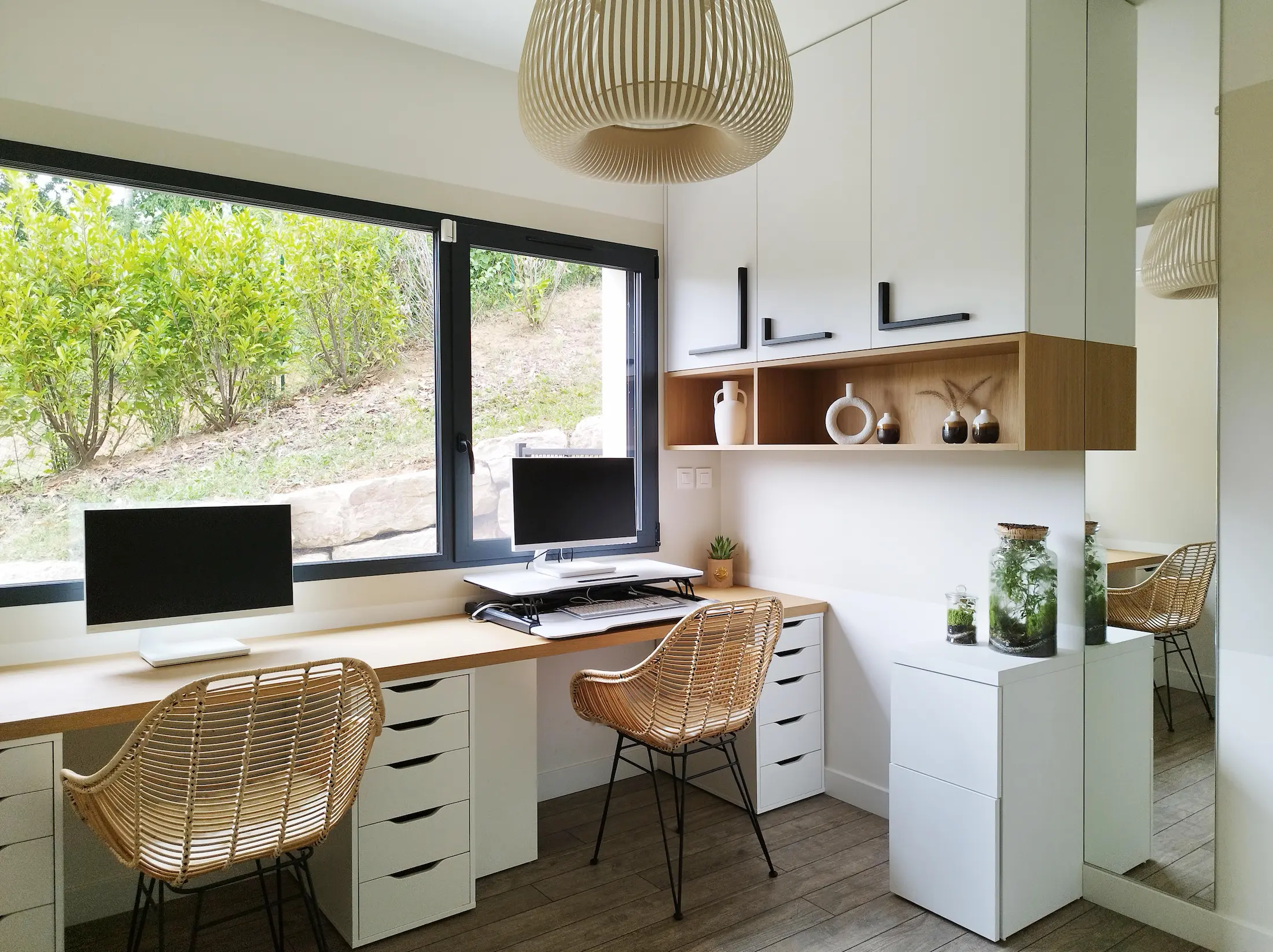 Aménagement de deux postes de travail face à une grande fenêtre, combinant bois naturel et rangements blancs.