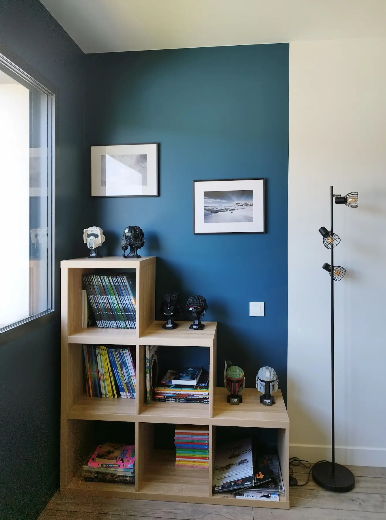 Coin lecture avec une bibliothèque en bois à modules déstructurés, posée contre un mur bleu ton sur ton.