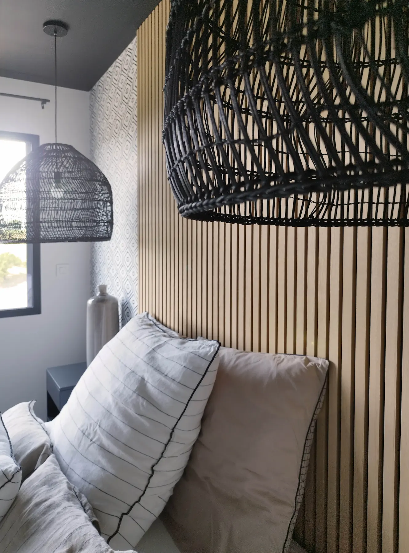 Gros plan sur la tête de lit en tasseaux de bois et luminaires suspendus noirs, apportant chaleur et relief.
