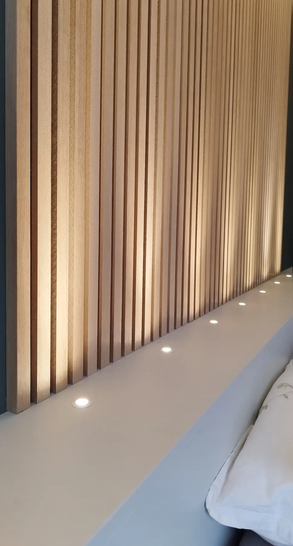 Ligne de spots intégrés sous les tasseaux bois créant une lumière douce et chaleureuse.