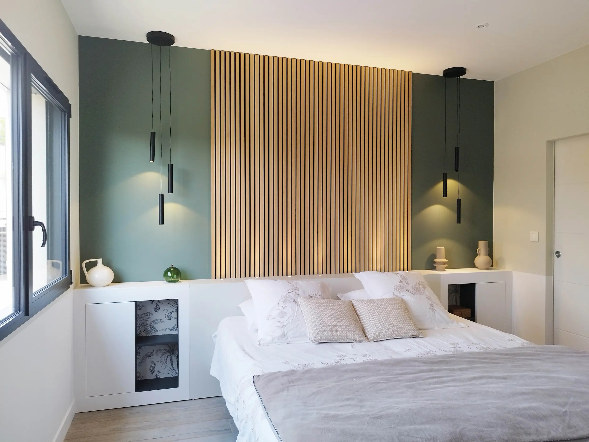 Chambre parentale lumineuse avec grande tête de lit en tasseaux, suspensions noires et mobilier intégré.