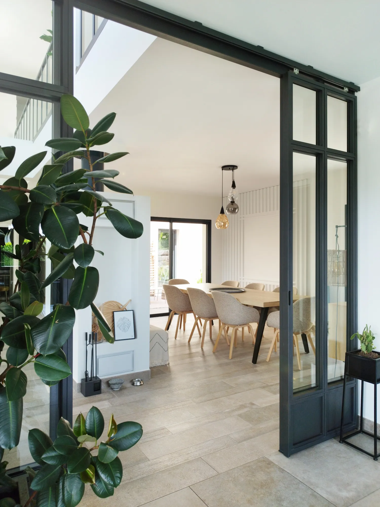Entrée lumineuse avec grande verrière noire menant à la salle à manger dans un style intérieur-extérieur harmonieux.